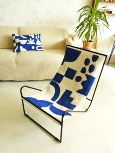 a blue and white chair sitting in front of a couch next to a potted plant