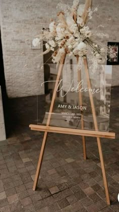 an easel with flowers on it and the word welcome is displayed in front of a brick wall