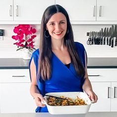 a woman in a blue dress is holding a bowl of food and smiling at the camera