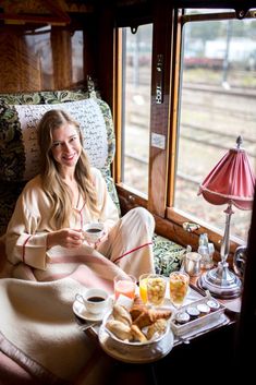 a woman sitting in a train car with food and drinks on the table next to her