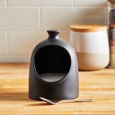 an empty black bottle sitting on top of a wooden table next to some spices and spoons