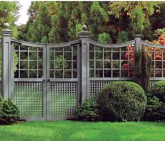 a gray gate with latticed windows in the middle of some bushes and trees behind it