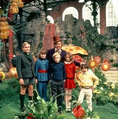 a group of people standing next to each other in front of flowers and plants with an umbrella