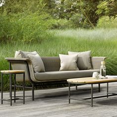 a couch and two tables on a wooden deck in front of tall grass with trees