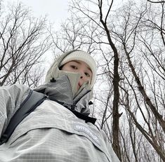 a person standing in front of some trees wearing a jacket and hat with the hood up