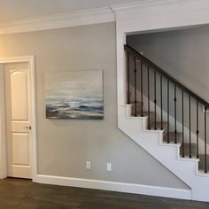 an empty living room with stairs leading up to the second floor, and a painting on the wall