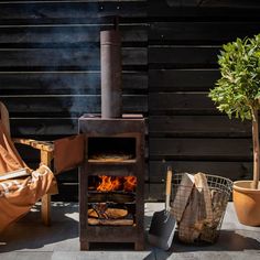 an outdoor wood burning stove with potted plants in the foreground and chairs around it