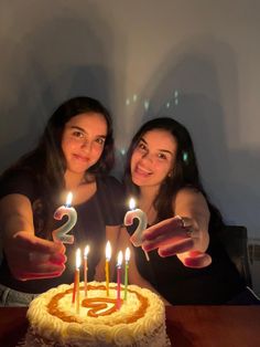 two women sitting in front of a birthday cake with candles on it and the number 2 spelled out