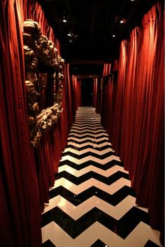 a room with red curtains and black and white chevrons on the floor in front of a mirror