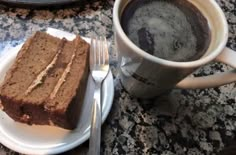 a piece of cake on a plate next to a cup of coffee