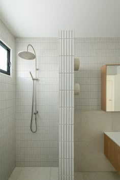 a white tiled bathroom with a shower head and mirror above the sink, in front of a window