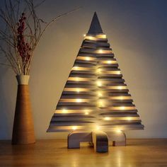 a lighted christmas tree next to a vase with branches in it and lights on the top