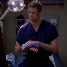 a man in scrubs sitting on a hospital bed next to a woman who is looking at him