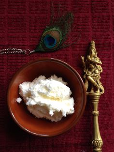 a bowl with whipped cream next to a peacock feather on a red table cloth and a golden spoon