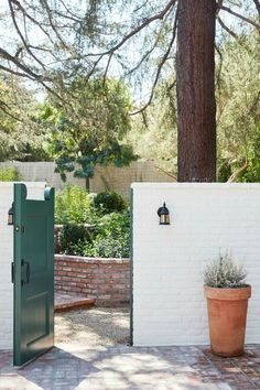 an open green door in front of a white brick wall and potted planter