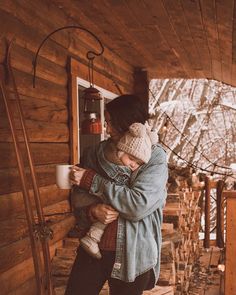 a woman holding a child in her arms while standing on the porch of a cabin