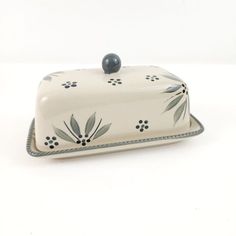 a white and blue ceramic covered dish with flowers on the front, sitting on a white surface