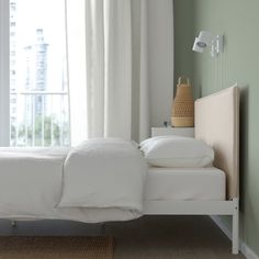 a white bed sitting next to a window in a room with green walls and curtains