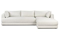 a white sectional couch with pillows on the back and foot rest in front of it