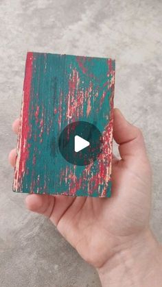 a hand holding up a small piece of wood that has been painted green and red