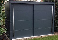 an outdoor storage shed in the middle of a garden with grass and bushes around it