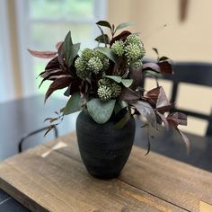 a black vase filled with flowers on top of a wooden table