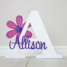 a wooden sign with the letter a and a flower on it's side in front of a wall