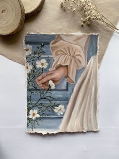 an image of a painting on paper with flowers and leaves around it, next to a piece of wood