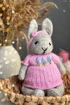 a knitted bunny in a pink dress sitting on a basket next to some flowers