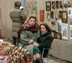 two women sitting on chairs in front of a table with many pictures and decorations behind them