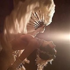 a woman with white hair and feathers on her head standing in front of a mirror