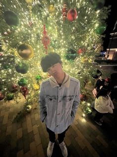 a young man standing in front of a christmas tree with lights on it's branches