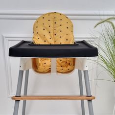 a yellow and black baby high chair next to a potted plant