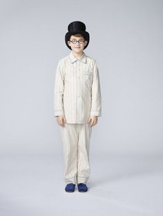 a young boy wearing glasses and a hat standing in front of a gray background with his hands on his hips