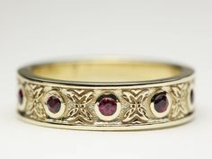 a close up of a wedding ring on a white surface with a red stone in the center