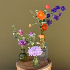 three vases filled with different types of flowers on a wooden table next to a brown wall