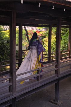 a woman in a kimono is sitting on a bench under a shelter with her back turned to the camera