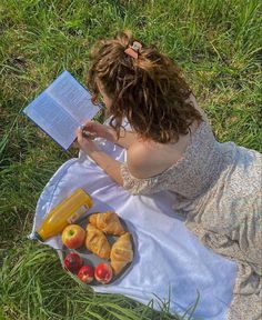 a woman sitting on the grass reading a book and eating food from a plate with croissants