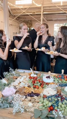 a group of women standing around a table covered in food and desserts while eating