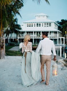 a man and woman walking on the beach holding hands with a lantern in front of them