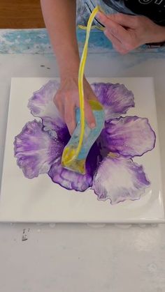 a person is painting a flower on a piece of white paper with yellow and purple paint