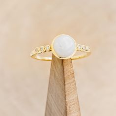 a gold ring with a white stone in the middle on top of a wooden stand