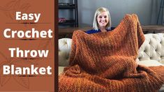 a woman is sitting on a couch holding up a crochet throw blanket in orange