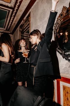 three women standing in a room with one holding up her hand and the other raising her arm