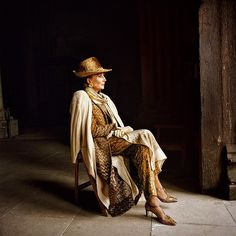 a woman wearing a hat and sitting on a chair in front of a doorway with her legs crossed