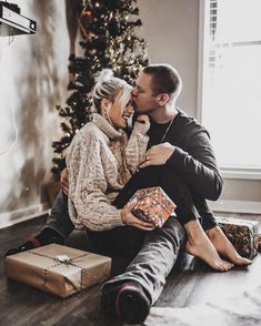 a man and woman sitting next to each other on the floor near a christmas tree