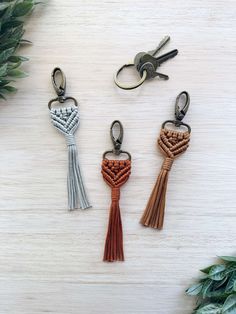 three keychains with tassels on top of a wooden table next to plants