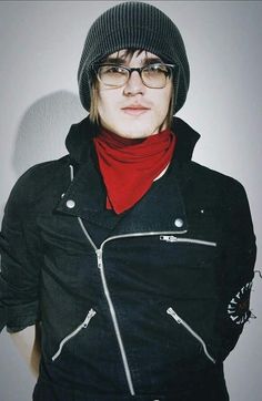 a woman wearing glasses and a black jacket with a red scarf around her neck is standing in front of a white wall