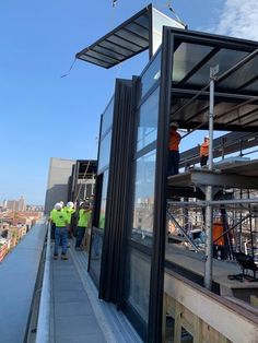 two men standing on the side of a tall building next to another man in yellow vests