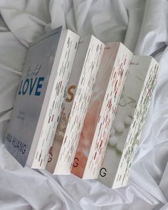 three books sitting on top of a white bed next to each other in front of a white sheet